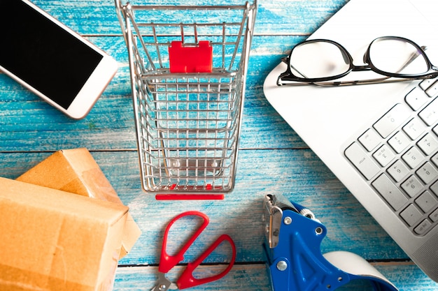 Online business concept.  Shopping cart with boxes and smartphone on table