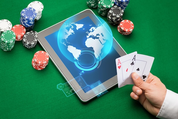 online casino, worldwide gambling, technology and people concept - close up of poker player with playing cards, tablet pc computer and chips at green casino table