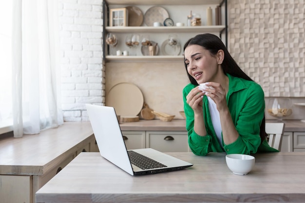 Online consultation with a family psychologist a young beautiful woman in the kitchen cries in