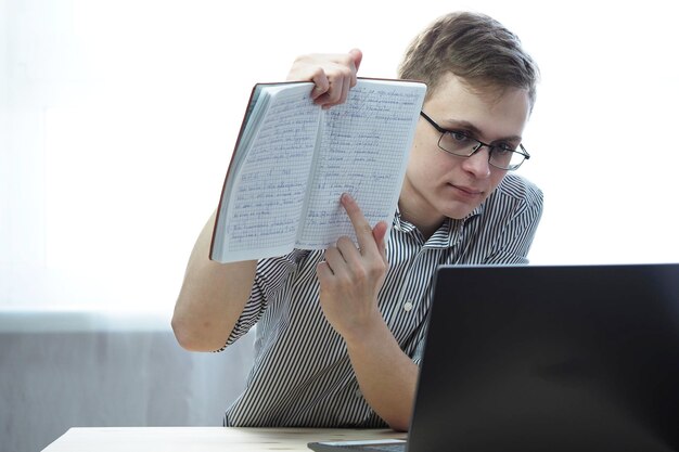 Photo online education a student with glasses behind a laptop with a notebook high quality photo