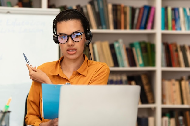 Online education Young teacher having video conference with students talking to laptop webcam sitting in library