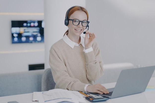 Online interpreter Young happy woman in headset is talking to client in front of laptop