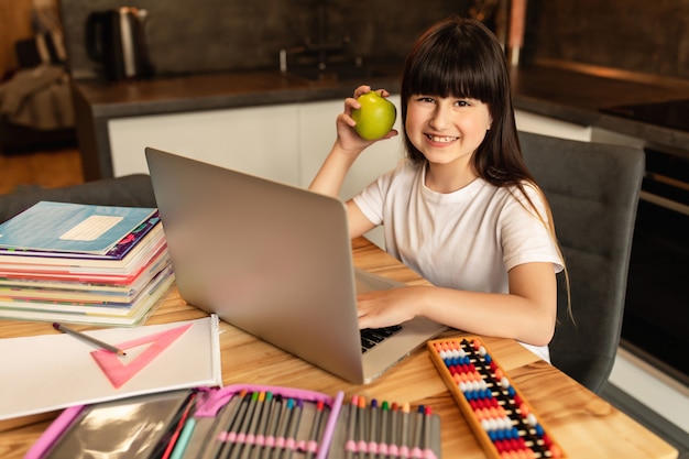 Online learning. Schoolgirl with green apple does homework at home