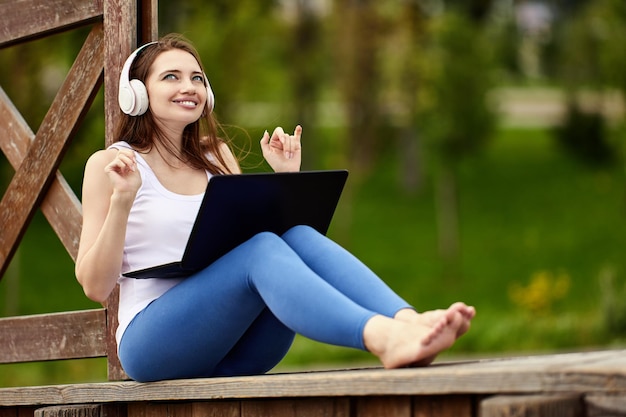 Online meeting in nature by cheerful woman in cordless headphones with laptop outside