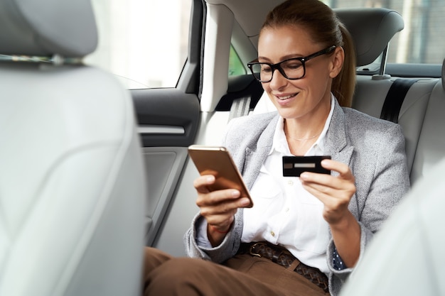 Online payment smiling business woman wearing eyeglasses using her smartphone and credit card to