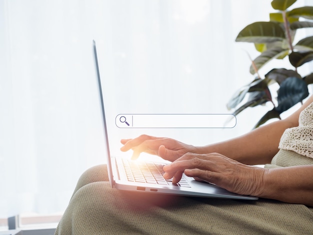 Online searching concept Empty blank search bar with magnifying glass icon appear while hands of senior woman using laptop computer Elderly female with internet Older people and technology