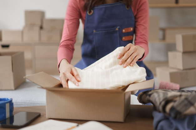 Online shopping business concept Women entrepreneur packing clothes in box for delivery to client