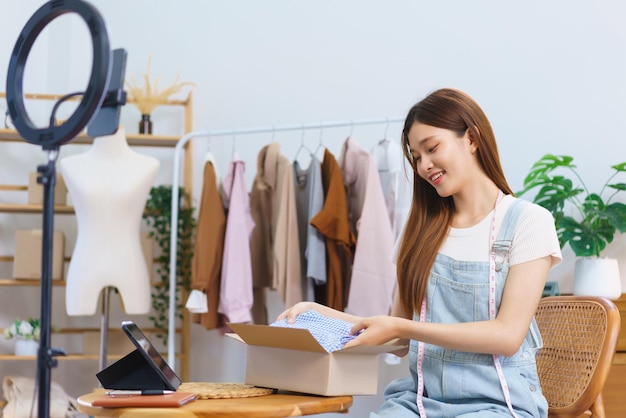 Online shopping concept Asian women packing dress in parcel box after live stream selling clothes