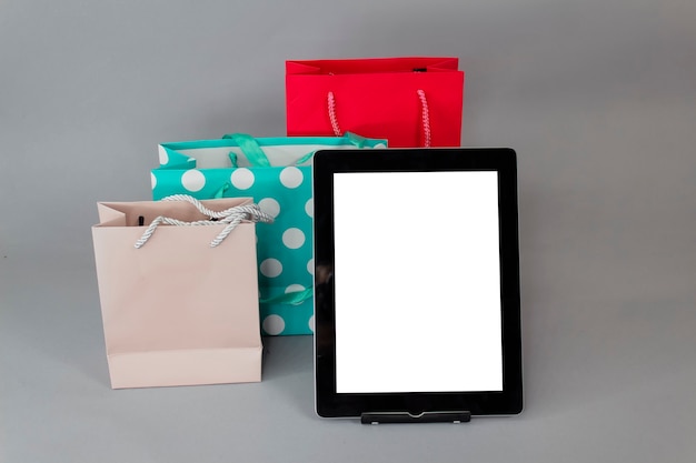 Online shopping concept. Close-up tablet mockup with white screen with bright gift bags on gray background.