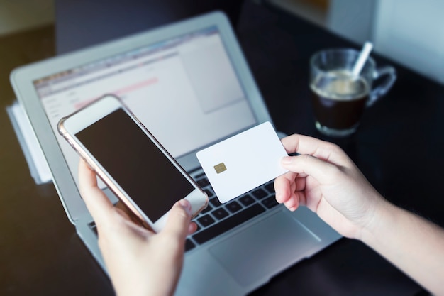 Online shopping concept. Closeup hand holding mobile and credit card with laptop on table 