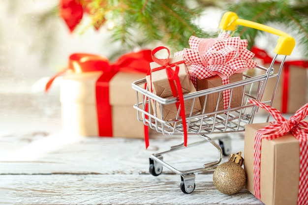 Online shopping concept - full Shopping Cart and gift boxes. Trolley full of different Christmas gift boxes with red ribbon on white wooden background.