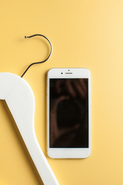 Online shopping concept. mobile phone and clothes hanger on a yellow background.