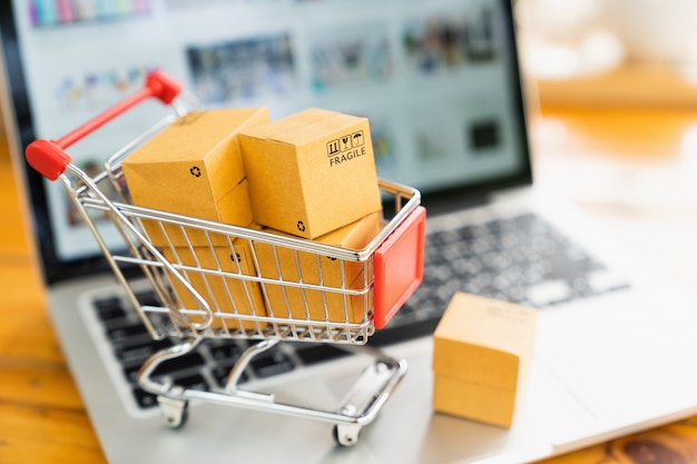 Online shopping and delivery concept, product package boxes in cart and laptop computer.