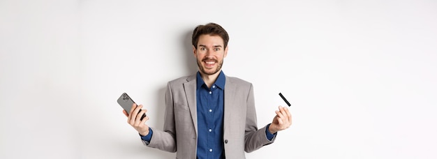 Online shopping excited man making money smiling amazed holding smartphone and credit card standing