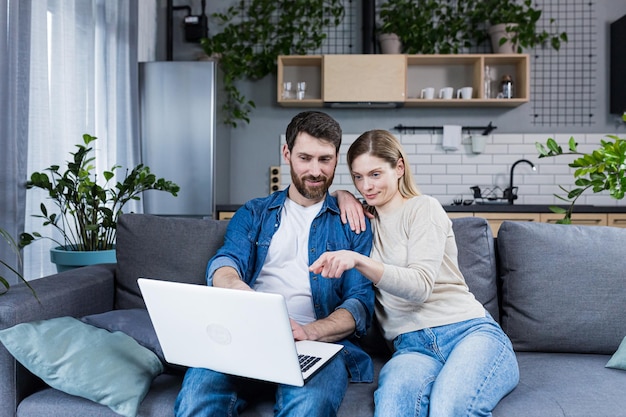 Online shopping Family man and woman at home sitting on the couch buying goods online from a laptop holding a credit card in their hands Happy smiling hugging