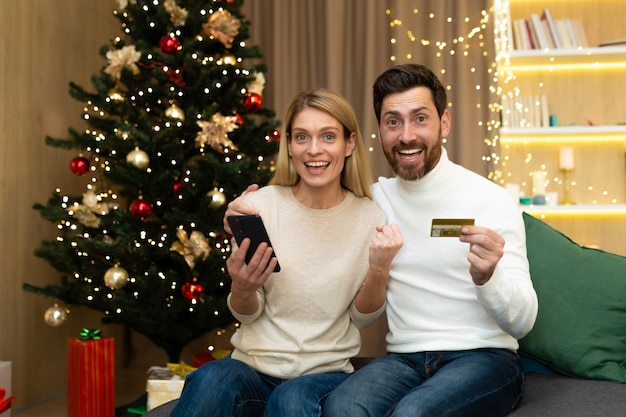 Online shopping happy young couple at home near the christmas tree a man and a woman hold a credit