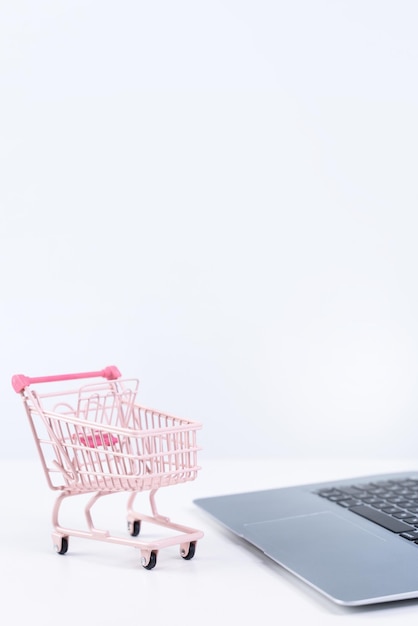 Online shopping Mini empty pink shop cart trolley over a laptop computer on white table background buying at home concept close up