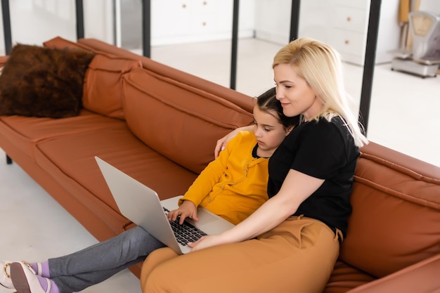 Online shopping or payments concept. Mother teaches his daughter using laptop at home. Sitting on the couch.