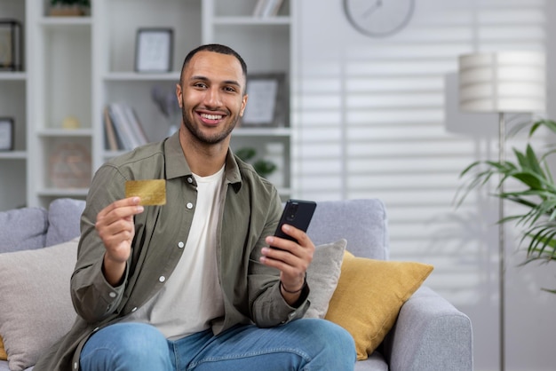 Online shopping portrait of a young african american man is sitting on the couch at home holding a