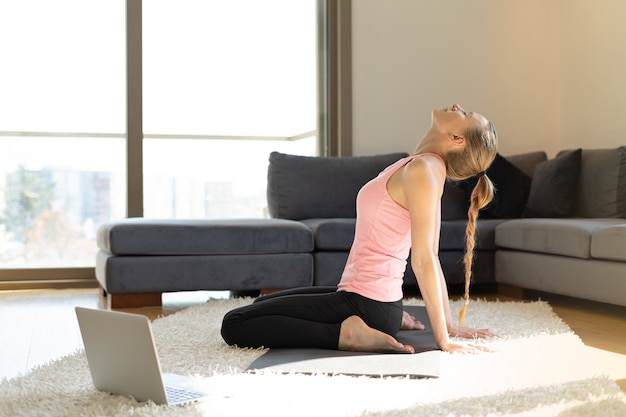 Online sport. young woman doing exercises on yoga mat opposite laptop