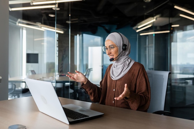 Online teaching young muslim woman in hijab and headset teacher sitting at desk in office in front