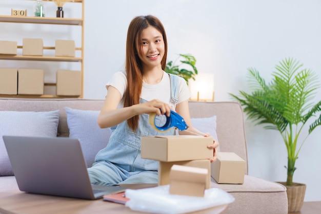 Online trader concept Female entrepreneur is packing products and sealing parcel boxes with tape