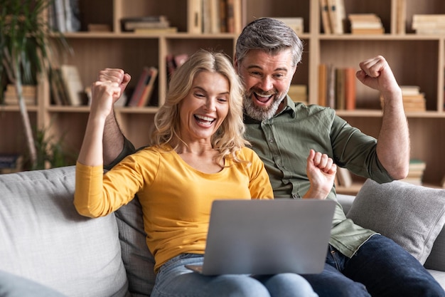 Online Win Portrait Of Overjoyed Middle Aged Couple Celebrating Success With Laptop