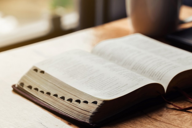 Open bible with a cup of coffee for morning devotion on wooden table 