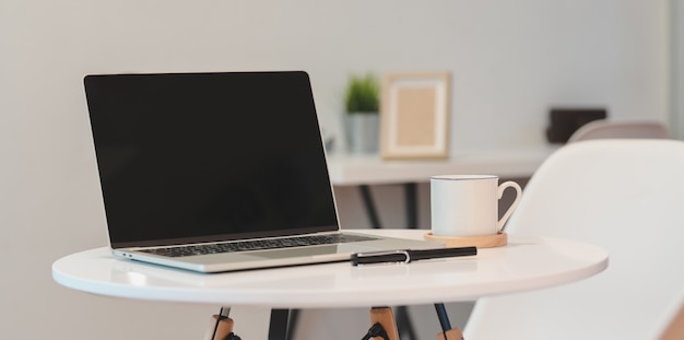 Open blank screen laptop computer in minimal workplace with coffee cup