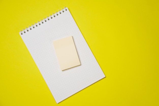 Open blank white notepad on a spiral and stickers on a yellow background