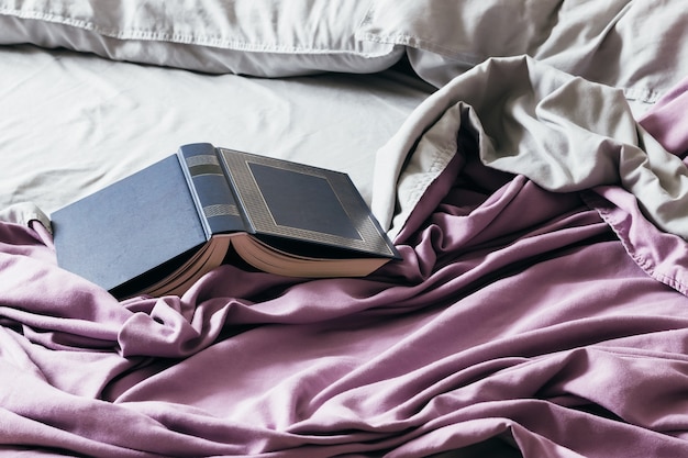 Open book on bed with a purple bedspread and gray pillows