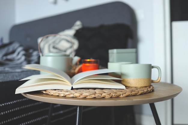 An open book a cup of tea a kettle and a candle on the background of the bed in the bedroom home interior