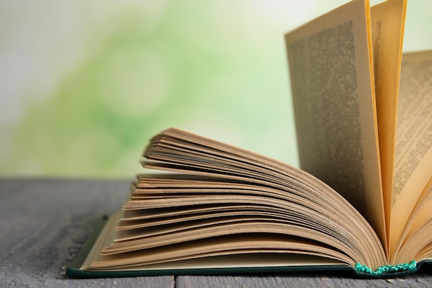 Open book on grey wooden table against blurred green background closeup