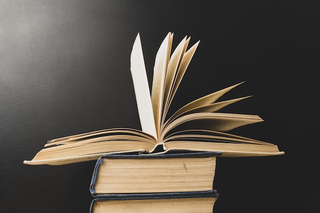 An open book lies on a stack of books on a black surface. Education.