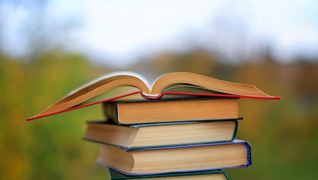 An open book lying on a stack of books in on a wooden table against the background of the garden.