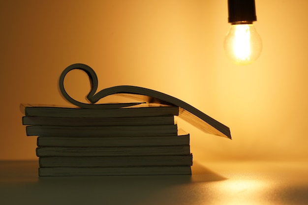 open book on pile of books under light bulb in orange background