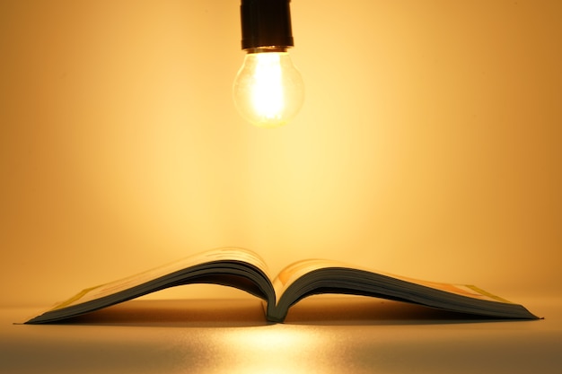 open book on table under light bulb in orange background