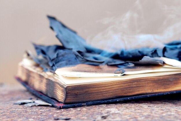 An open book with burnt charred pages and smoke on the table Burning of banned literature