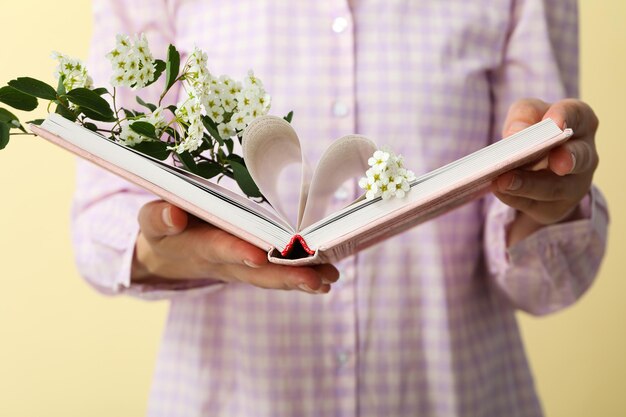 Open book with flowers in female hands on yellow background