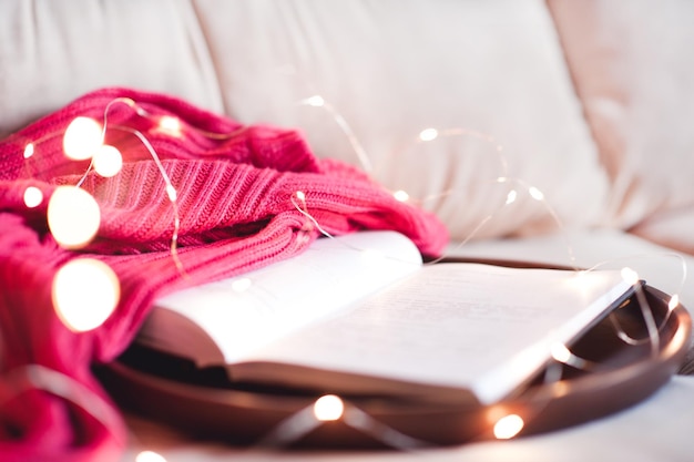 Open book with knitted sweater on wooden tray in bed closeup Good morning