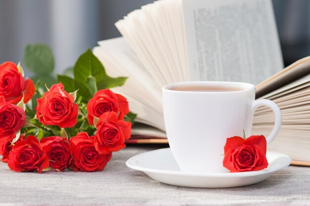 An open book with red orange roses and a cup of tea. Reading and relaxing. Romantic, sweet, dating concept.