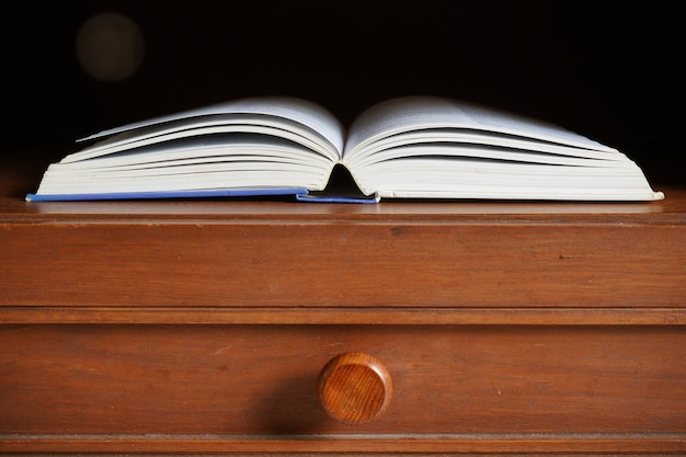 Open book in wooden cabinet shelf with empty dark room background