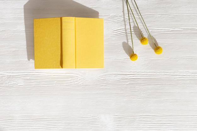 Open book in yellow cover and flowers on white wood Concept of reading books and time without gadgets