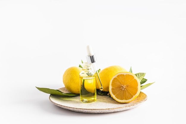 An open bottle of cosmetic natural remedy based on lemon essential oil stands on a ceramic plate and ripe lemons organic cosmetics