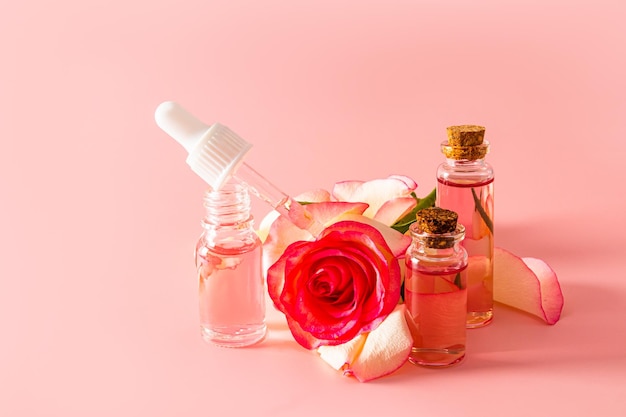 An open bottle of rose oil and an oilfilled pipette rose water in glass bottles with a stopper on the background of a rose flower natural care