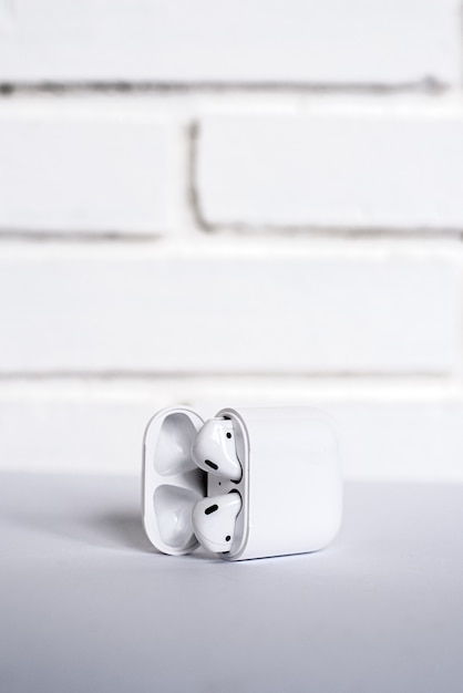 Open box with modern true wireless earbuds placed on table against white brick wall