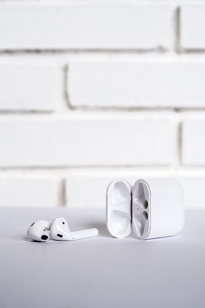 Open box with modern true wireless earbuds placed on table against white brick wall