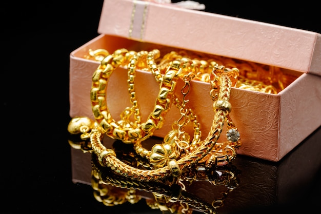 Open box with pile of various golden jewelry, isolated black background.