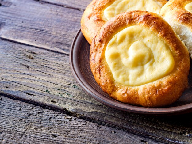 Open buns with cottage cheese (vatrushka) lying in a clay plate on a wooden table.  