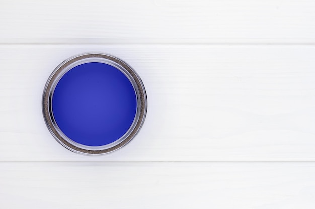 Open can with blue paint on a white wooden background top view with copy space